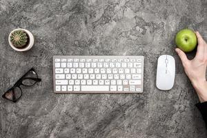 Top view keyboard, glasses, mouse and a fresh green apple in male hand photo