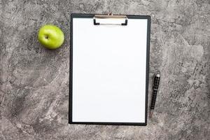 Top view empty white blank paper next a pencil and a fresh green apple on the plaster background photo