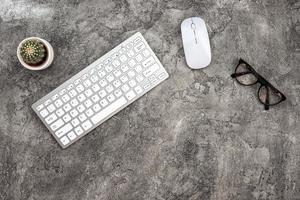 Top view plaster background with keyboard, glasses, mouse and a cactus. - Copyspace photo