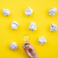 male hand holding a bulb on yellow background. crumpled paper is scattered nearby photo