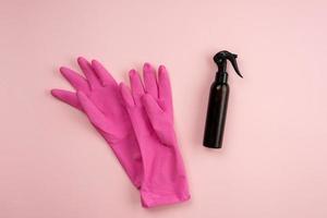 guantes de látex rosa y spray en la botella sobre un fondo rosa. concepto de servicio de limpieza foto