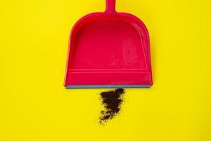 Sweep litter from the floor . Sweeps coffee into a red scoop on a yellow background. Simple cleaning photo