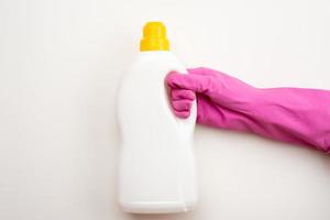 Close up of female hand in pink gloves holds white bottle with place for text isolated on white background. Cleaning supplies concept. Copy space for ad. photo