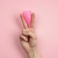 Close up of woman hand holding menstrual cup over pink background. Women health concept, zero waste alternatives photo