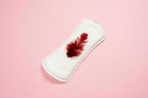 Menstruation. White woman lying on pink background. Female lining with red feather. Women's critical days. photo