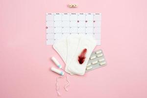 Tampon, feminine, sanitary pads for critical days, feminine calendar, pain pills during menstruation and a red feather on a pink background. Care of hygiene during menstruation.