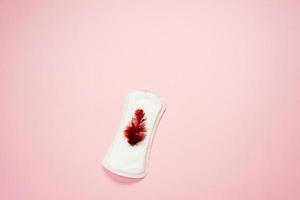 Woman pad lying isolated on pink background with red feather on it . Woman hygiene protection sanitary photo