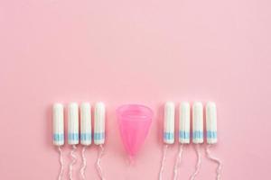 Reusable silicone menstrual cup and heap of tampons comparison on a soft pink background. Modern female intimate alternative gynecological hygiene. Eco zero waste concept. Copy space place for text photo