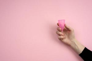 mano sostiene un cuenco vaginal sobre un fondo rosa. Remedios para los días críticos. foto