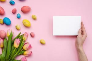 huevos de pascua y tarjeta de saludos sobre fondo rosa foto