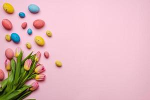 Easter background with colorful eggs and yellow tulips over wood. Top view with copy space