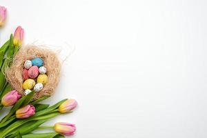 Easter background, multi colored eggs and bouquet of tulips lie on a white table. - Copy space photo