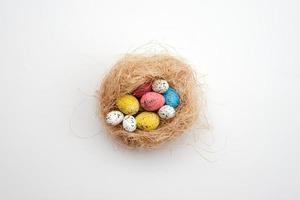 Fondo de Pascua, huevos multicolores en un nido yacen sobre una mesa blanca