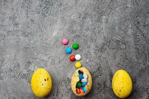 Multi-colored candies in the yellow egg  on a grey plaster background. - Copyspace photo