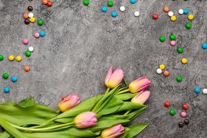 Easter background with a multi-colored candy and tulips on a grey plaster background