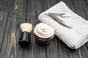 Image of shaving tools, brush, foam, shaver on dark, wooden background photo