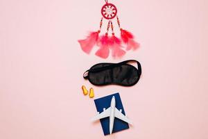 On a pink background are things for travel, passport, airplane, blindfold, earplugs, amulet photo