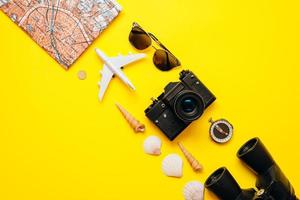 On a yellow background on a diagonal important things are laid out sunglasses, binoculars, the camera, the map photo