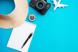 concepto de vacaciones de verano, sobre fondo azul sombrero, cuaderno, bolígrafo, brújula y avión foto