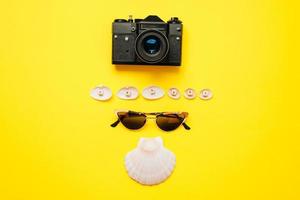 Sunglasses, a vintage camera and seashells are laid out on a yellow background. Leisure concept photo