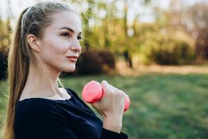 Beautiful strong athletic girl doing exercise, training outdoor. Concept of healthy active sport fitness life. Young sexy muscle woman with dumbbells. Practicing workout, gym outside. photo