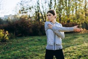 mujer joven estirando y calentando en el parque. chica atractiva que se extiende antes de la aptitud. hermosa chica deportiva haciendo fitness al aire libre. foto