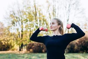 Beautiful young girl posing with dumbbell, outdoors, looking away. photo