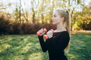 Profile of slim girl with dumbbells outdoors. Fitness in park. photo