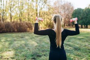 Fitness in the park, girl holding dumbbells, back view. photo