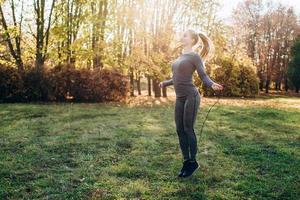 Sunny day, the girl in the park jumps on a skipping rope. photo