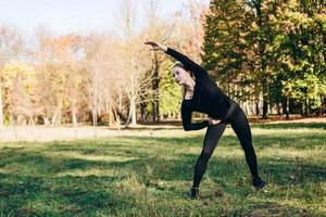 Girl in black sportswear performs exercise tilt left outdoors, autumn day. photo