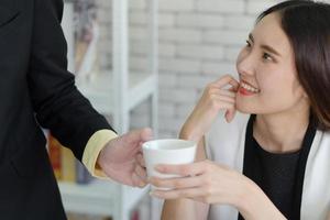 Businessman handing coffee to asian woman in office photo