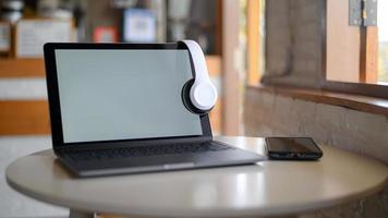 maqueta de pantalla en blanco de portátil y auriculares en pantalla, portátil colocado sobre una mesa en un café. foto