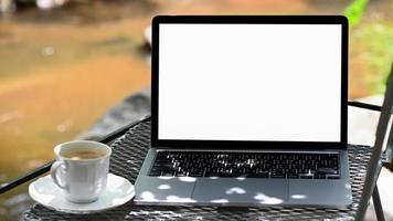 maqueta de pantalla blanca portátil y taza de café en la mesa con fondo de naturaleza.
