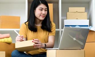 mujer mirando la pantalla del portátil y escribiendo la dirección en la caja del paquete, venta en línea, entrega de paquetes.
