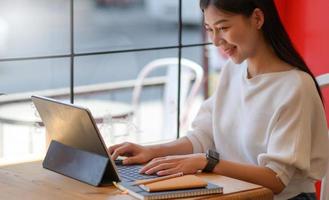 una mujer joven está operando una computadora portátil en un café con una expresión sonriente.