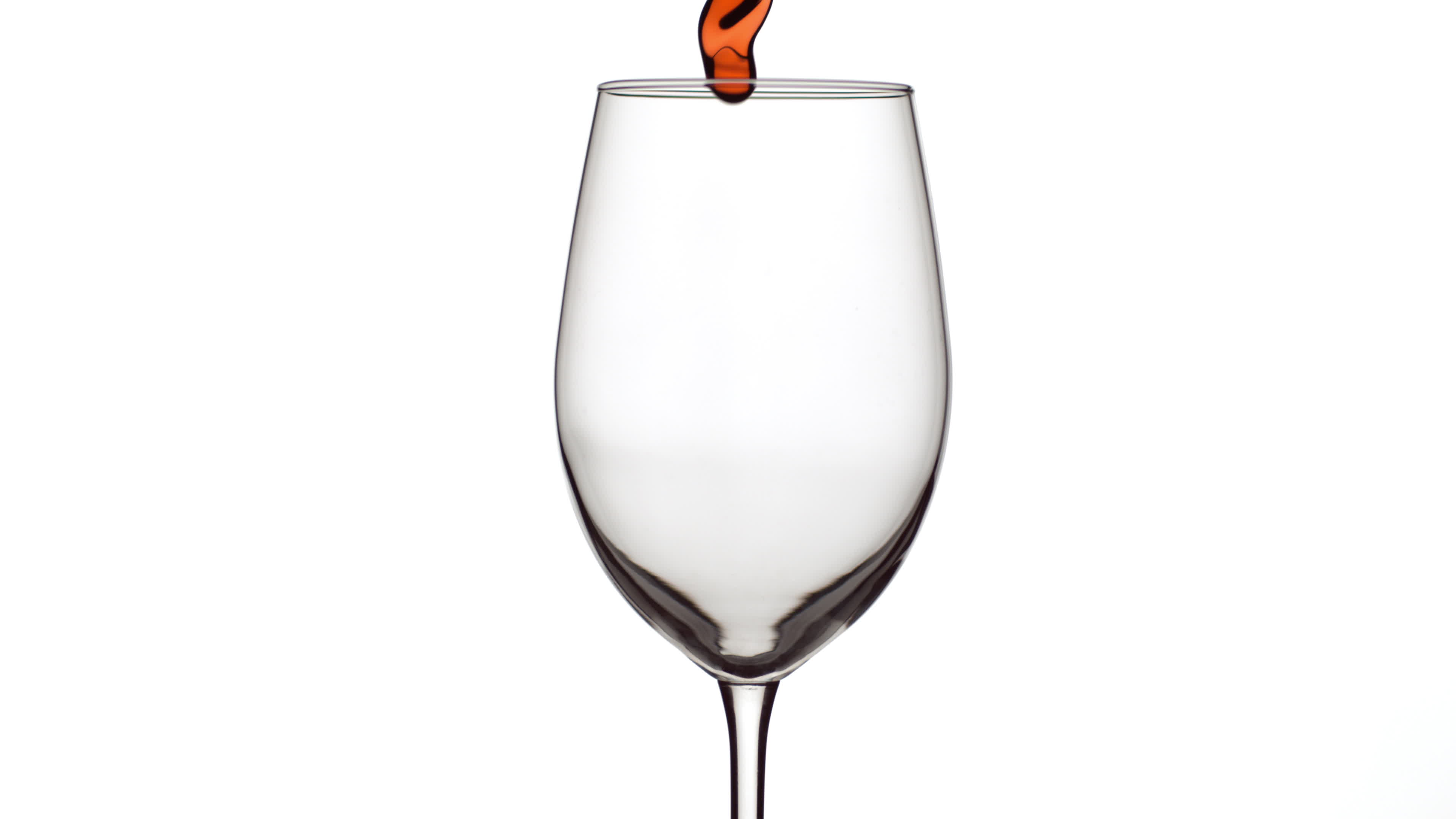 Slow motion shot of red wine pouring into glass on white background