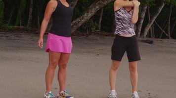 duas mulheres na praia se alongando e se preparando para correr. filmado em vermelho épico para alta qualidade 4k, uhd, resolução ultra hd. video