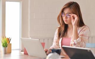 Cropped shot of A young woman wearing glasses is operating a laptop looks thinking. photo