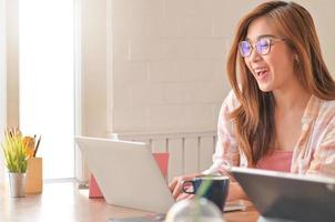 Toma recortada de una joven asiática usa una computadora portátil con una expresión feliz.