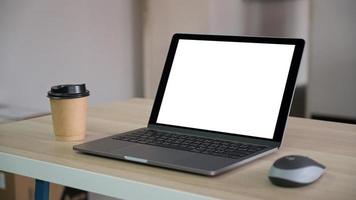 Portátil de pantalla en blanco con taza de café para llevar marrón sobre la mesa de la oficina.