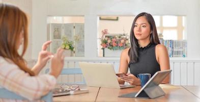 Young woman holds a smartphone in hand and laptop with tablet on the table.She and her friend are preparing a project to present a client. photo