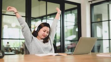 A teenage girl wears headphones with her arms up to relax during an online class.