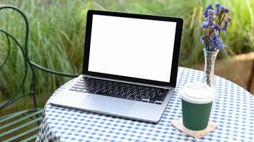 maqueta de pantalla en blanco de portátil blanco con taza de café para llevar sobre la mesa. foto