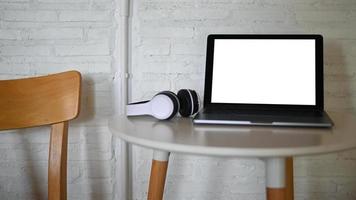 maqueta de pantalla en blanco de portátil y auriculares colocados sobre una mesa en un café.