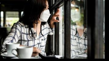 una mujer con una máscara médica sentada en un café mirando por la ventana. foto