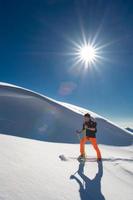 Un hombre esquiador alpino subir a esquís y pieles de foca en un fuerte día soleado foto