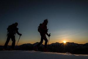 Los montañistas de esquí escalan montañas con esquí por la tarde al sol foto
