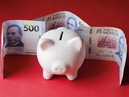 Hucha blanca y billetes mexicanos de 500 pesos sobre fondo rojo. foto