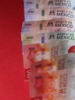 Filas de billetes mexicanos de diferente denominación sobre el fondo rojo. foto